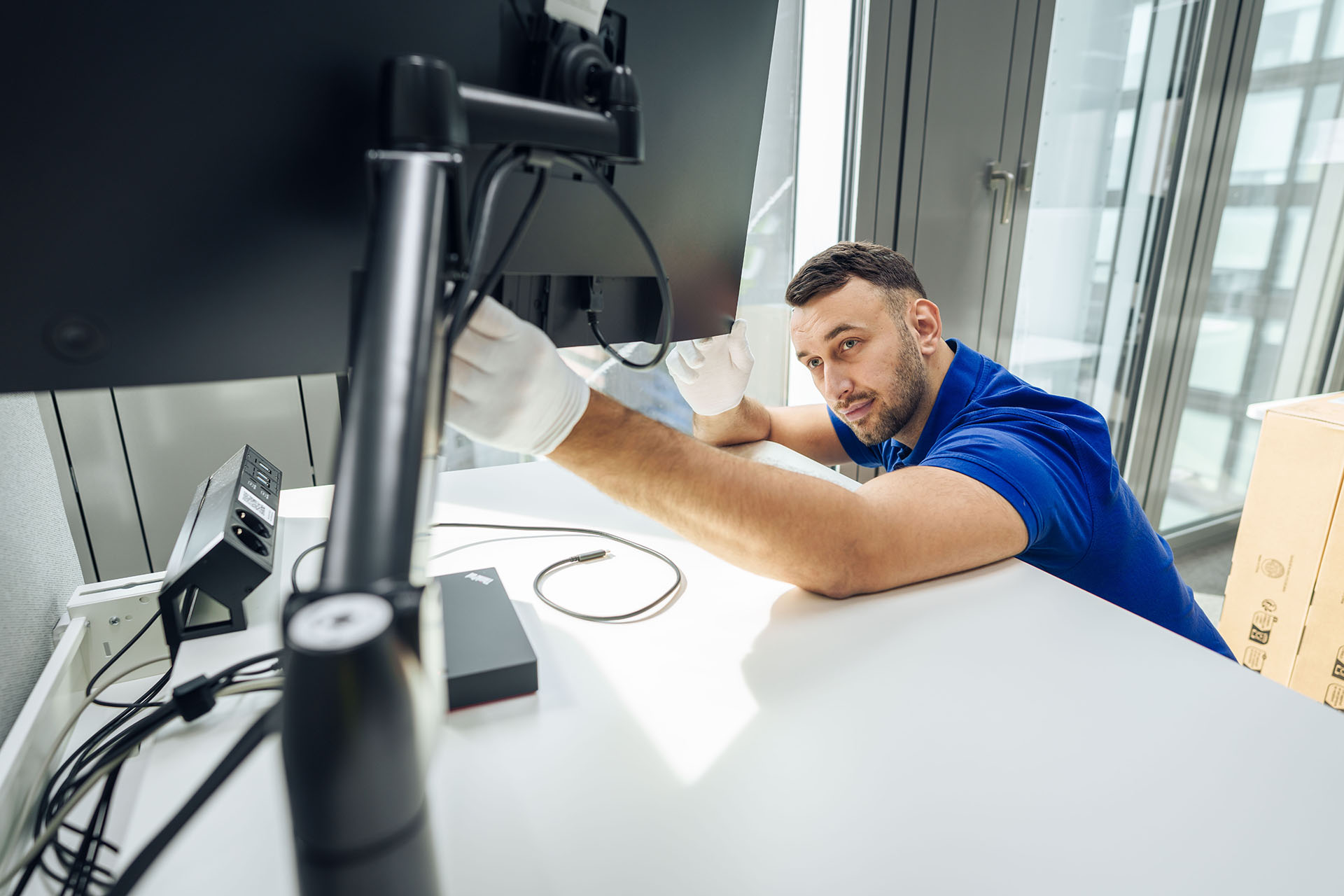 Techniker montiert einen Monitor und richtet Kabel sorgfältig aus, um die IT-Ausstattung in einem neuen Büro einzurichten.