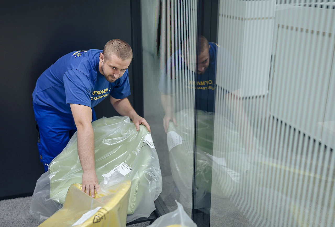 Mitarbeiter des Logistikunternehmens verpackt sorgfältig einen gepolsterten Bürostuhl in Schutzfolie für den internen Transport.