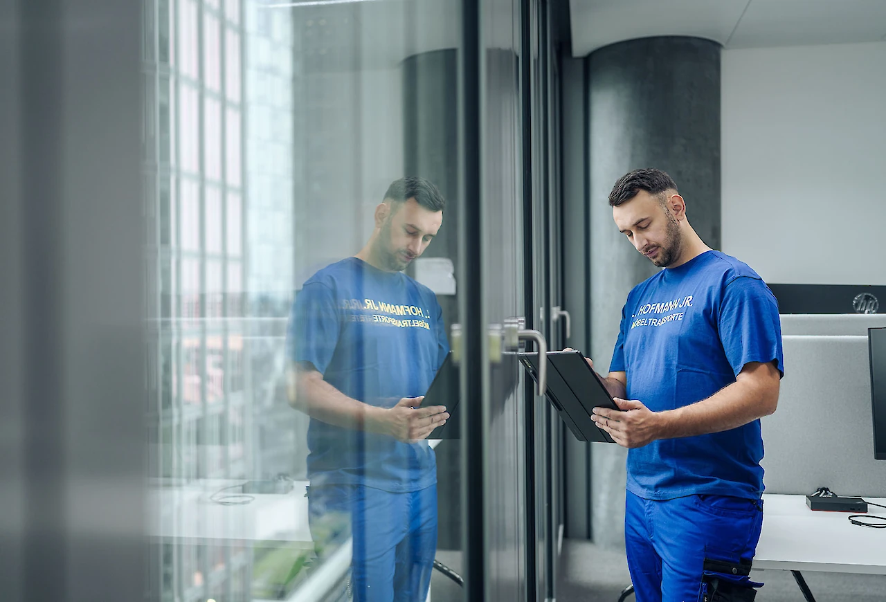 Ein Logistikmitarbeiter überprüft Details auf einem Tablet, er spiegelt sich im Fenster wieder.