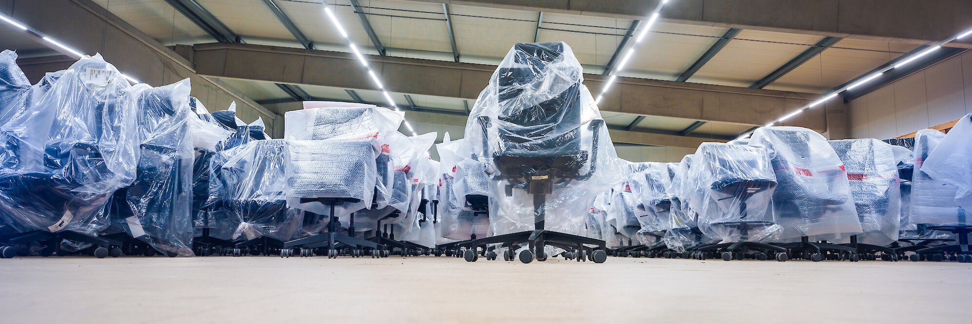 Mehrere Bürostühle sicher in Schutzfolien verpackt und ordentlich in einer Lagerhalle für die Möbellagerung arrangiert.