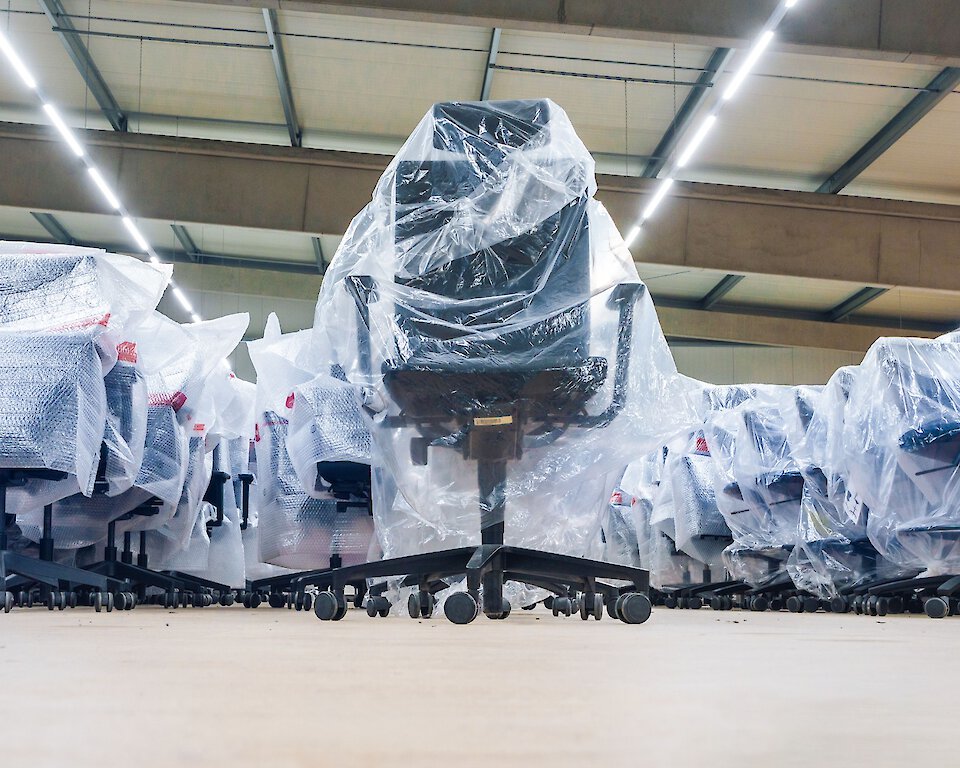 Mehrere Bürostühle sicher in Schutzfolien verpackt und ordentlich in einer Lagerhalle für die Möbellagerung arrangiert.