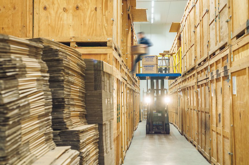 Gabelstapler transportiert Kartons zwischen großen Holzlagerboxen in einem organisierten Kleinlager.