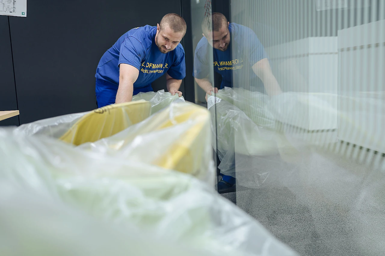 Hofmann-Mitarbeiter verpackt sorgfältig einen Bürostuhl in Schutzfolie.